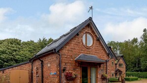 A brick building with a sloped roof, a round window, and a door with a glass panel. - Charming 2-bed Cottage, Beautiful Views, Knutsford (Knutsford)