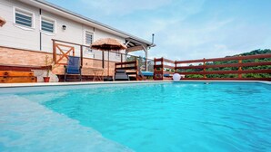 A swimming pool with a wooden deck, lounge chairs, and a thatched umbrella. - Charmante Villa Neuve à Trinité (La Trinité)
