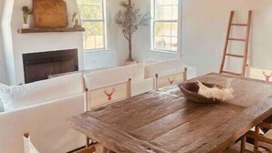 A rustic interior with a wooden dining table, white upholstered chairs, a fireplace, and a ladder against the wall. - A Sanctuary of Stories! (Round Top)