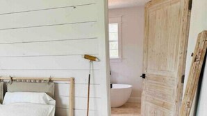 A bedroom with a bed, a wooden door, a wooden floor, and a white wall. - A Sanctuary of Stories! (Round Top)