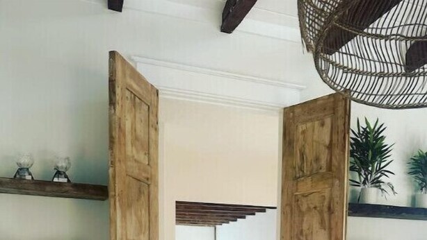 A hallway with wooden doors leading to a dining area, shelves with decorative items, and a hanging light fixture. - A Sanctuary of Stories! (Round Top)