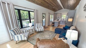 Ein geräumiges Wohnzimmer mit Holzbalkendecke, einem gestreiften Sofa, einem braunen Ledersessel, einem blauen Sofa und einem Essbereich mit Küche im Hintergrund.