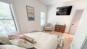 Ein Schlafzimmer mit einem Bett, einem Sessel, einer Kommode und einem Fernseher an der Wand.