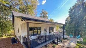 Einbungalow mit überdachter Veranda, einer kleinen Terrasse und einem Patio mit Gartenmöbeln.
