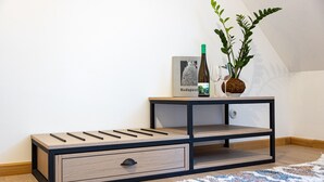 A corner of a room with a wooden and metal nightstand, a framed picture, a bottle of wine, and a potted plant. - Czakó Bed & Breakfast (Budapest)
