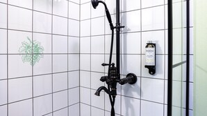A bathroom with white tiled walls, a black showerhead, and a bottle of shampoo on the wall. - Czakó Bed & Breakfast (Budapest)