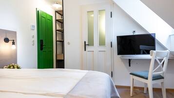 Quarto com cama, porta verde, televisão e escrivaninha com cadeira.