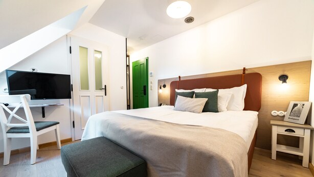 A bedroom with a bed, a desk, a chair, a nightstand, and a green door. - Czakó Bed & Breakfast (Budapest)