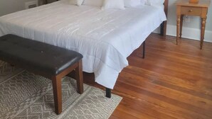 A neatly made bed with white linens, a wooden headboard, two bedside tables with lamps, a bench, and a patterned rug on a wooden floor. - 1895 meets 2023 Townhouse. (Hamilton)