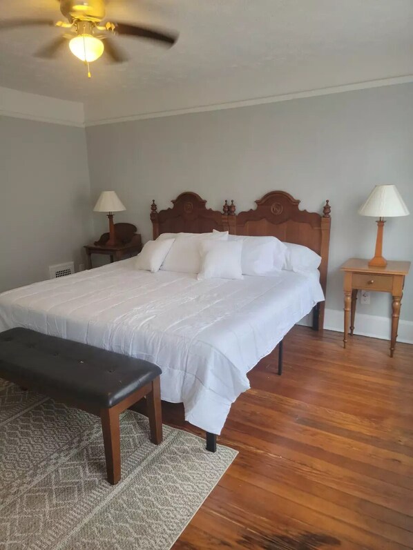 A neatly made bed with white linens, a wooden headboard, two bedside tables with lamps, a bench, and a patterned rug on a wooden floor.