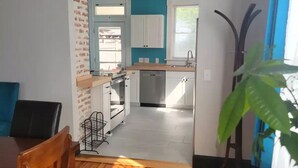 A modern kitchen with white cabinets, a wooden dining table, and a large plant. - 1895 meets 2023 Townhouse. (Hamilton)