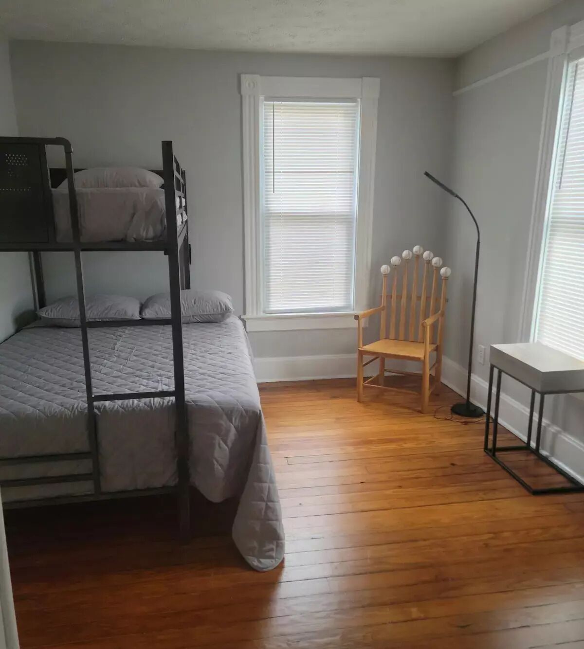 A room with a bunk bed, a wooden chair, a desk, and a floor lamp.