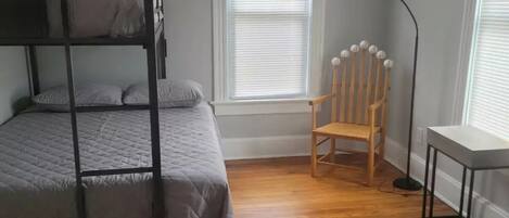 A room with a bunk bed, a wooden chair, a desk, and a floor lamp.