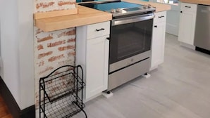 A kitchen with a brick accent wall, a blue wall, and a stainless steel oven. - 1895 meets 2023 Townhouse. (Hamilton)