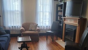 A living room with a sofa, armchair, coffee table, and fireplace. - 1895 meets 2023 Townhouse. (Hamilton)