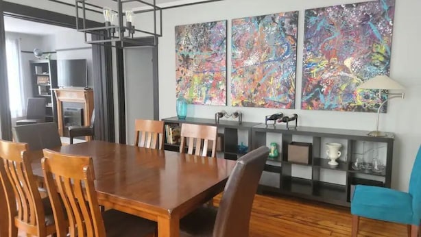 A dining area with a wooden table and chairs, a black metal ceiling light, and a wall with abstract paintings. - 1895 meets 2023 Townhouse. (Hamilton)