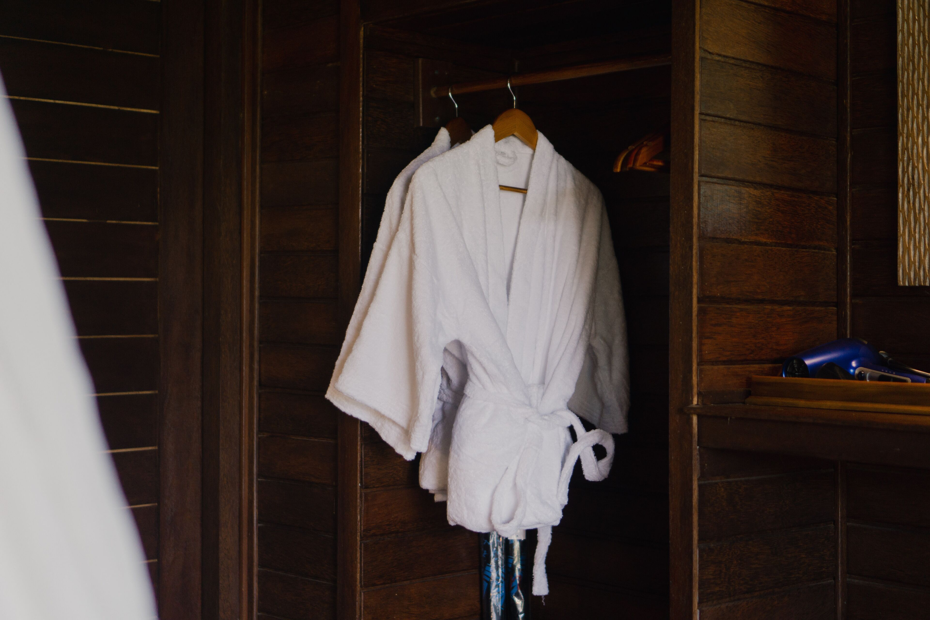 Un intérieur en bois, avec une robe blanche suspendue à un cintre en bois.