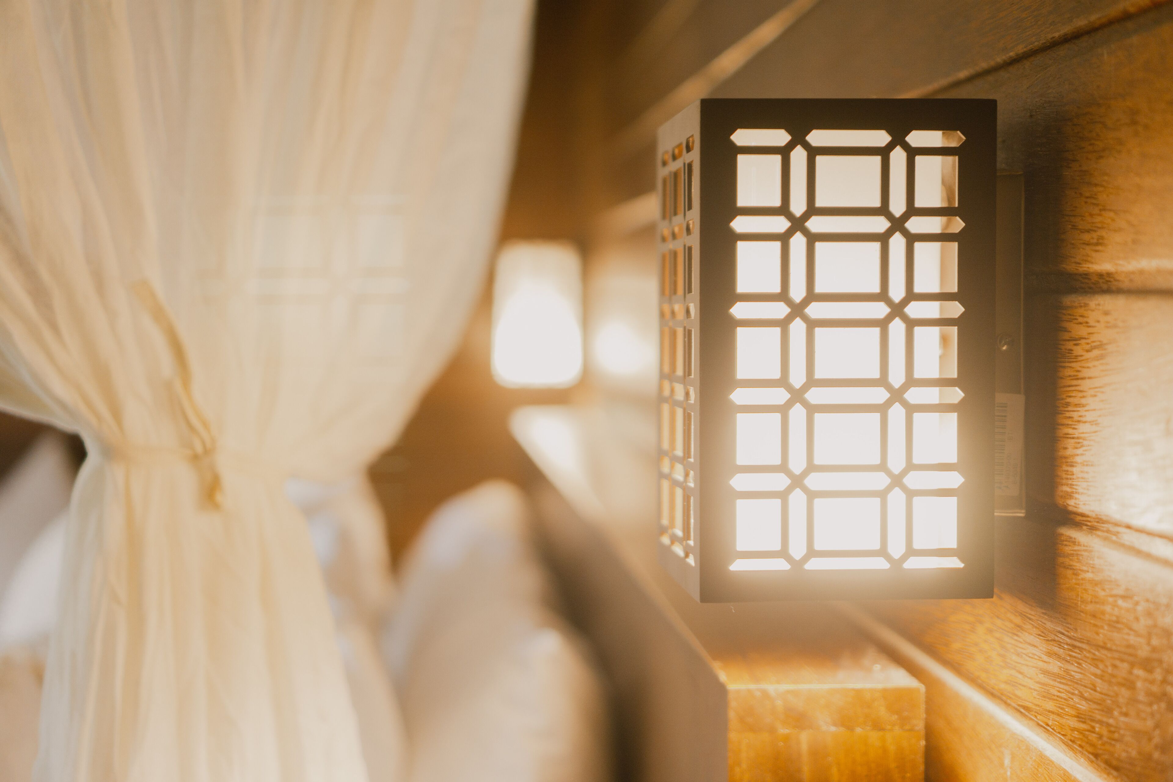 A room with a bed, a window with a geometric pattern, and a wooden headboard.