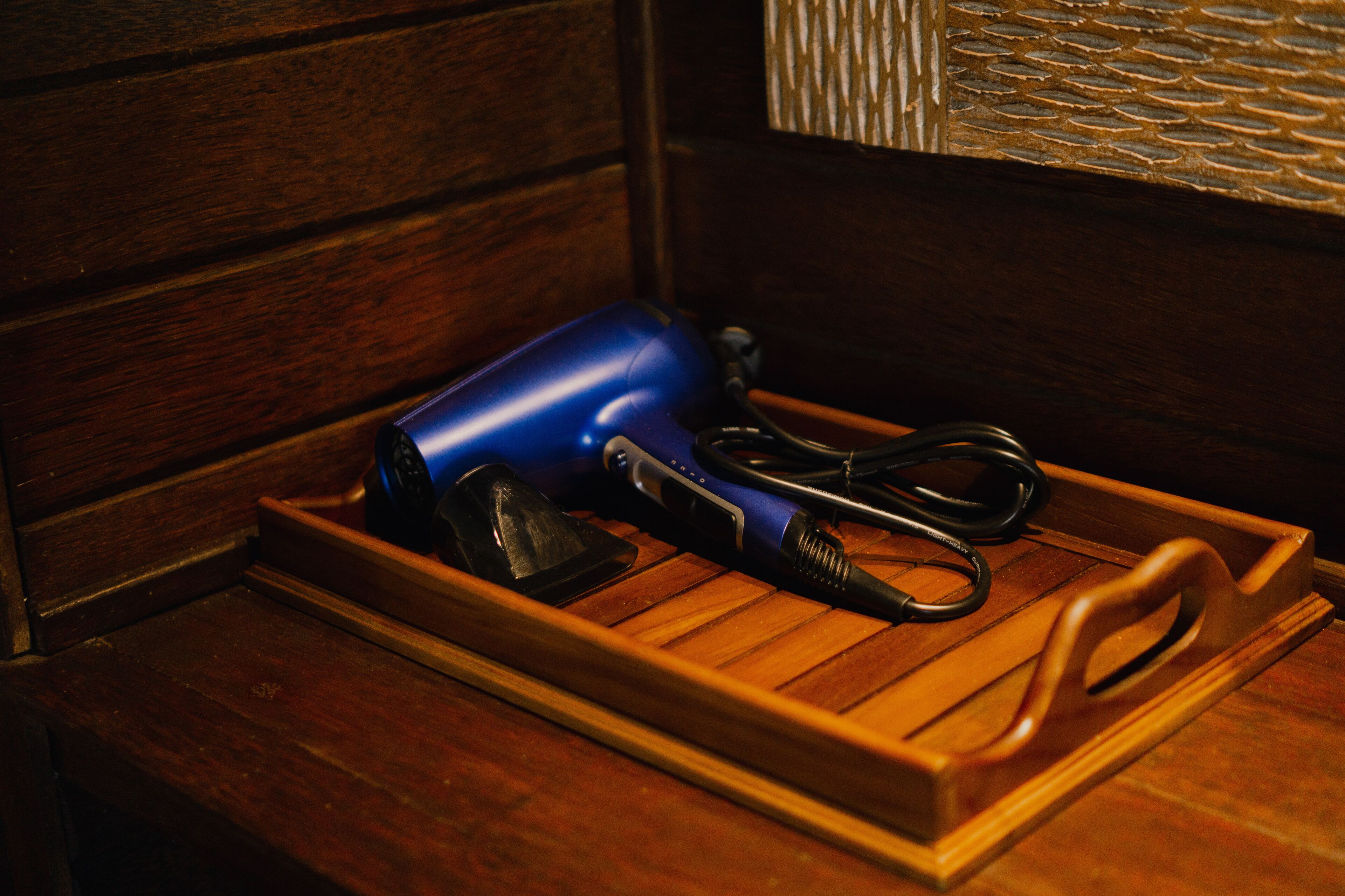 A wooden tray with a blue hairdryer, a black vacuum cleaner, and a pair of scissors on a wooden floor.