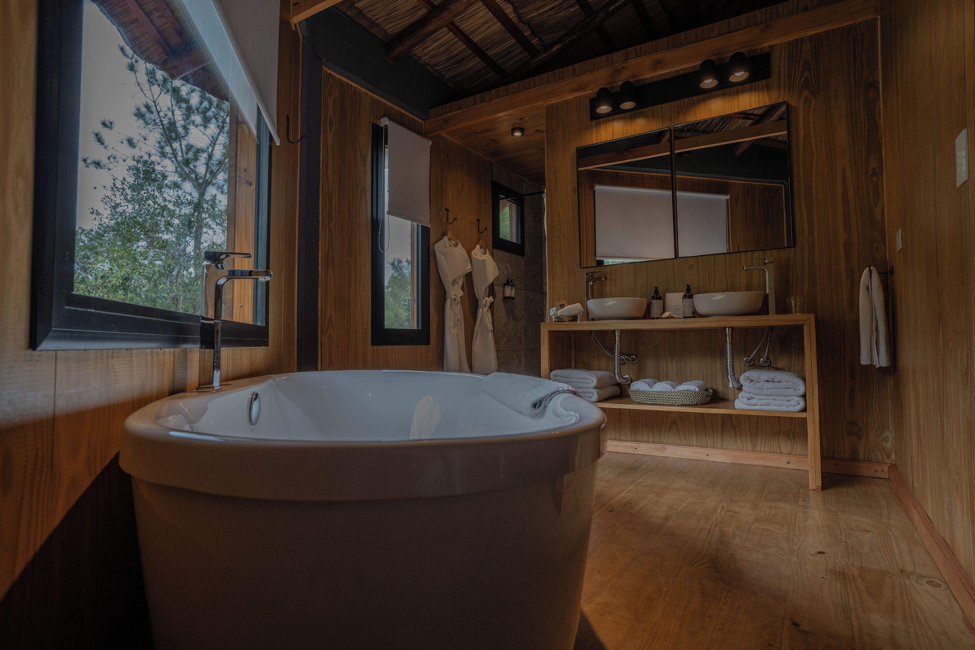 A wooden bathroom with a freestanding bathtub, a large mirror, and a shelf with towels.