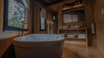 A wooden bathroom with a freestanding bathtub, a large mirror, and a shelf with towels.