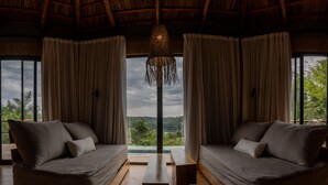 A room with two sofas facing each other, a hanging light fixture, and large windows offering a view of greenery. - Reserva Natural Iguazú - Pristine Luxury Camp (Puerto Libertad)