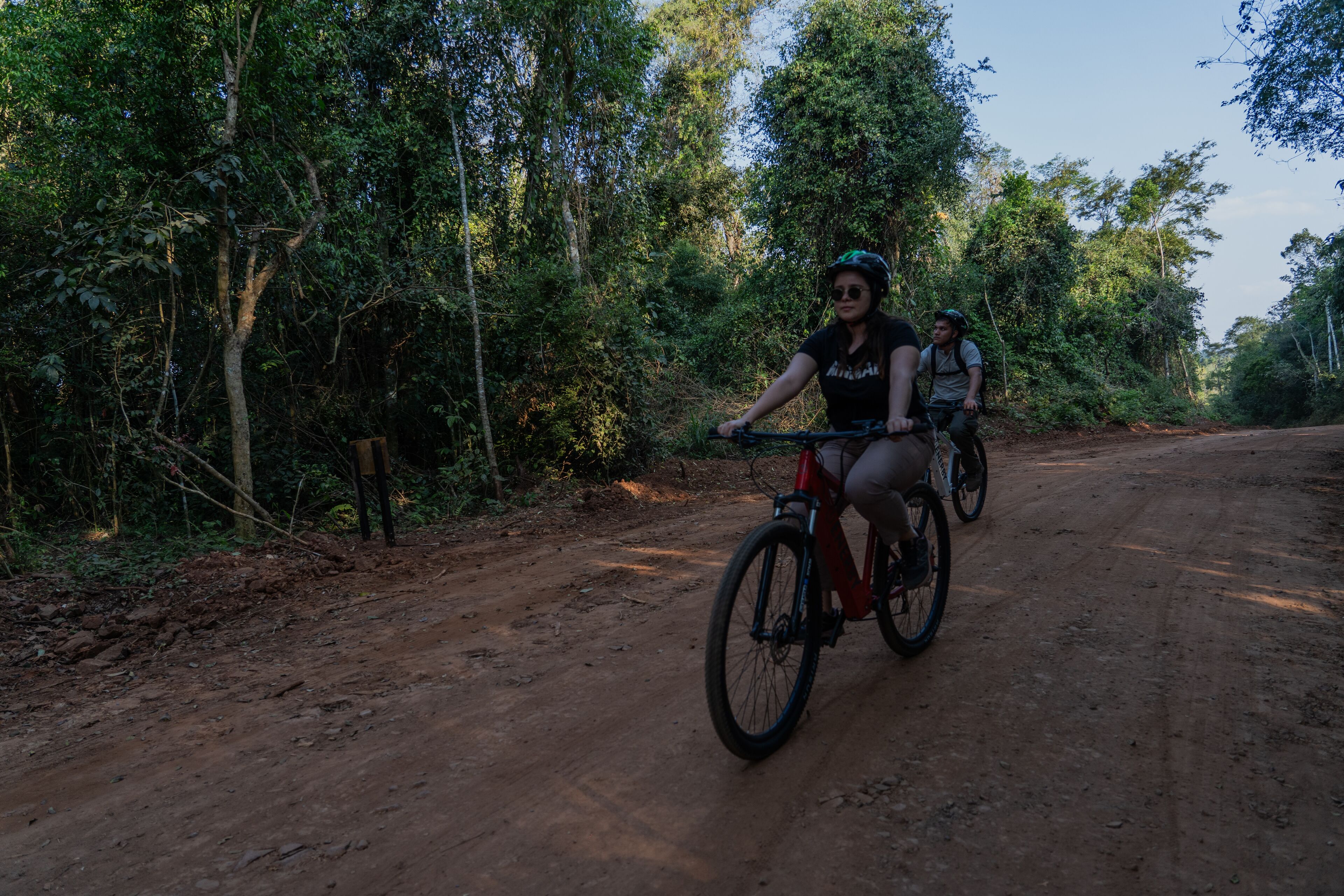 Two people on a dirt path surrounded by dense forest.
