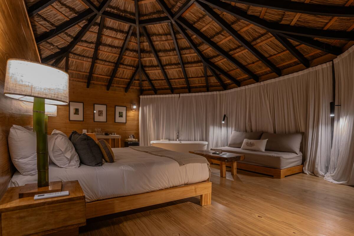 Une pièce avec un plafond en bois, un lit, un canapé, une table et une lampe.