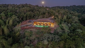 An aerial view of a lodge surrounded by dense forest, with a swimming pool and a well-lit building. - Reserva Natural Iguazú - Pristine Luxury Camp (Puerto Libertad)