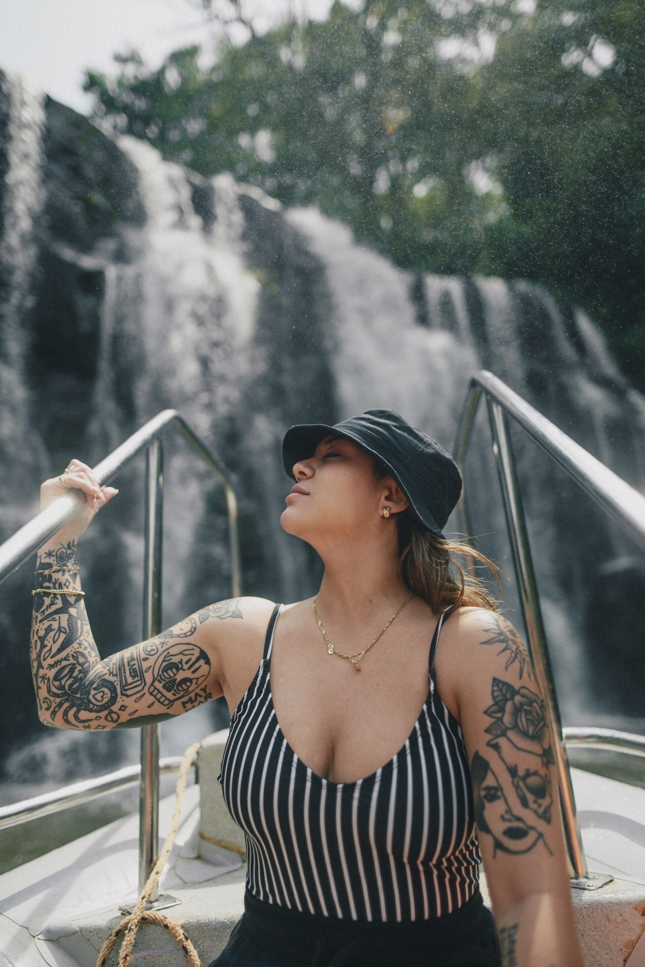 Una persona con tatuajes de pie en un bote, con una cascada al fondo.