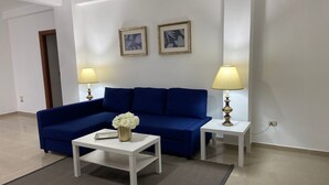 Ein Wohnzimmer mit einem blauen Sofa, zwei weißen Beistelltischen, einem weißen Couchtisch und zwei Lampen.