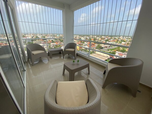 A balcony with wicker furniture, a small table, and a view of a cityscape.