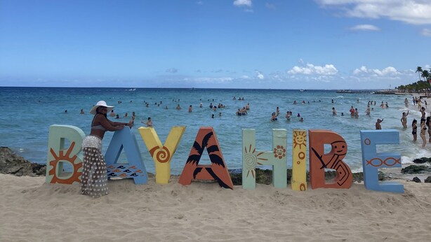 Ein Strand mit bunten Buchstaben, die „DAYVALE“ buchstabieren, und Menschen, die im Wasser schwimmen.