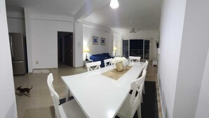 Ein Essbereich mit einem weißen Tisch und Stühlen, einer blauen Couch und einem Kühlschrank im Hintergrund.