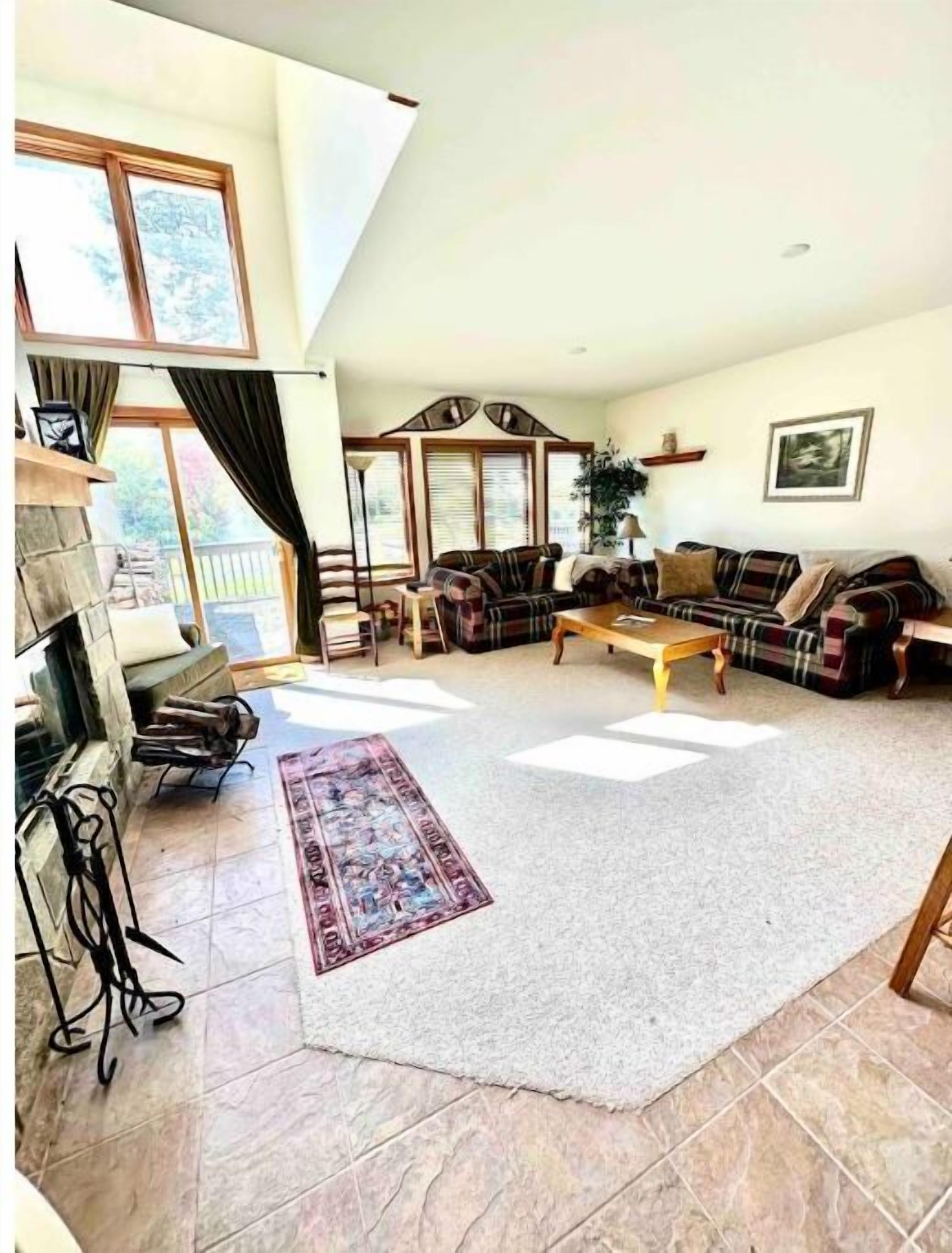 A spacious living room with a fireplace, large windows, and a high ceiling.