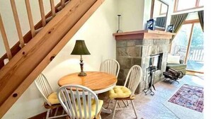 Comedor con mesa y sillas de madera, chimenea de piedra y una escalera.