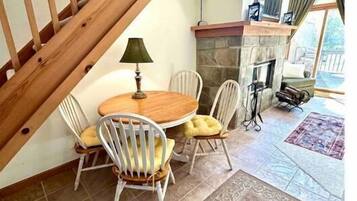 Comedor con mesa y sillas de madera, chimenea de piedra y una escalera.