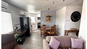 A living room with a sofa, armchair, and a ceiling fan. There is a dining area with a table and chairs.