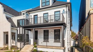 A two-story house with a balcony, a front porch, and a small garden area. - New Luxe Reno W/Hot Tub & Roof Top Terrace! (Columbus)