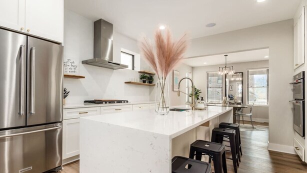 A modern kitchen with stainless steel appliances, a marble island, and black bar stools. - New Luxe Reno W/Hot Tub & Roof Top Terrace! (Columbus)