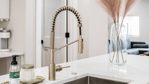 A modern kitchen with a stainless steel sink, a gold-colored faucet, and a clear vase with dried flowers on the counter. - New Luxe Reno W/Hot Tub & Roof Top Terrace! (Columbus)