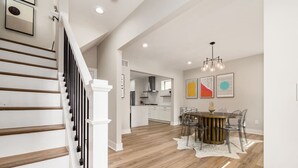 A spacious kitchen with modern appliances, a dining area with a round table and chairs, and a staircase with wooden steps and white railings. - New Luxe Reno W/Hot Tub & Roof Top Terrace! (Columbus)