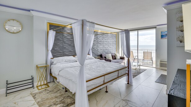Ein Himmelbett mit weißen Leinen, ein modernes Kopfstück und Meerblick durch große Fenster.
