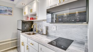 Eine moderne Küche mit weißen Schränken, goldenen Griffen, einem Edelstahl-Kühlschrank, einer Marmorarbeitsplatte und einem eingebauten Backofen.