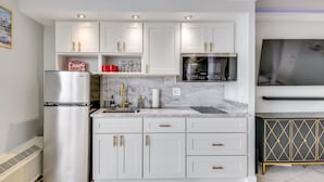 Eine moderne Küche mit weißen Schränken, goldenen Griffen, einem Edelstahl-Kühlschrank, einer Mikrowelle und einer Marmorarbeitsplatte.