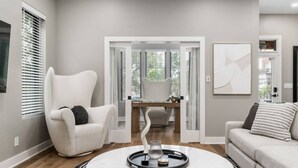 A modern living room with a white armchair, a sofa, a round coffee table, and a dining area with a table and chairs. - New Build Hot Tub Dtown ShortNorth (Columbus)