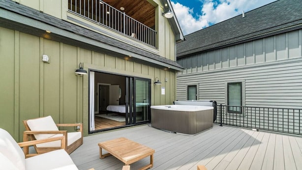 A deck with outdoor seating, a hot tub, and a bedroom visible through a sliding door. - New Build Hot Tub Dtown ShortNorth (Columbus)