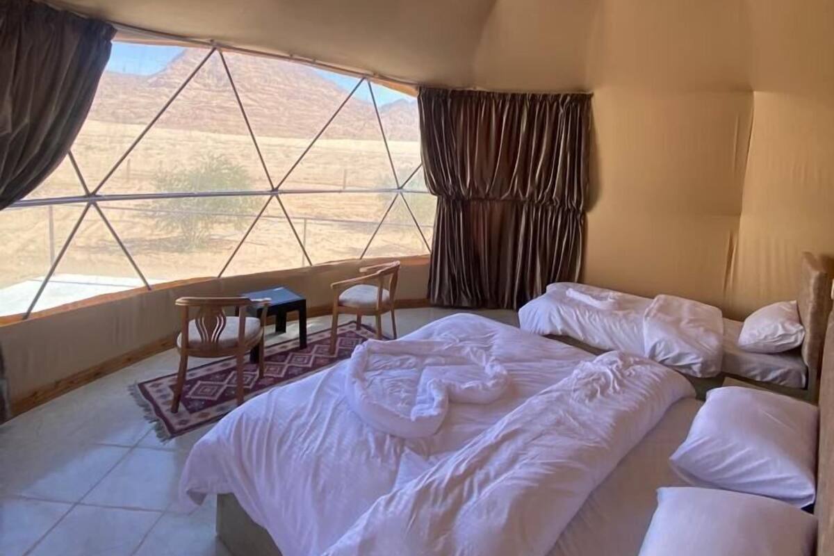 Un dormitorio con una cama grande, una mesita y una silla. Se ve el desierto a través de un ventanal amplio.