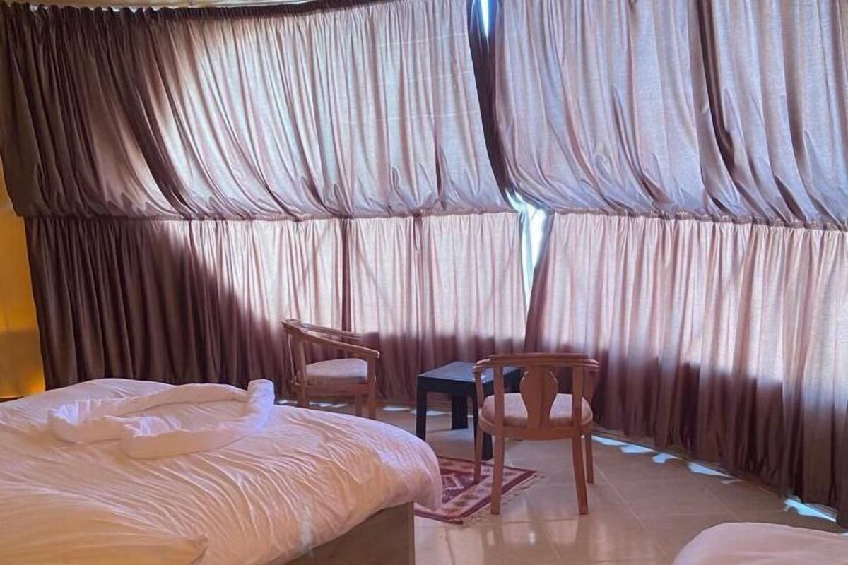 Una habitación de hotel con una cama grande, una cama más pequeña, una silla de madera y una mesita.