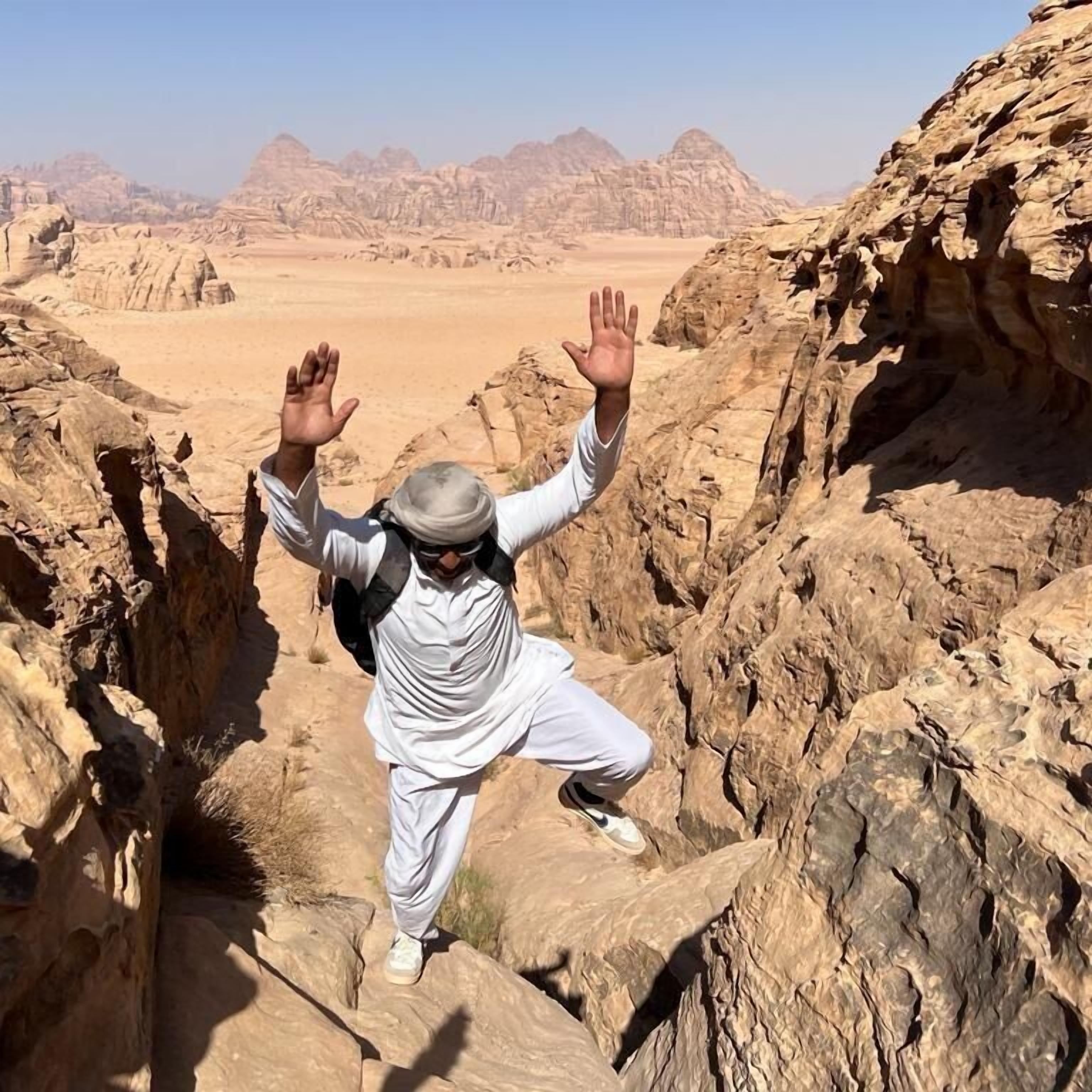 A person in white attire climbing rocky terrain with a desert landscape in the background.